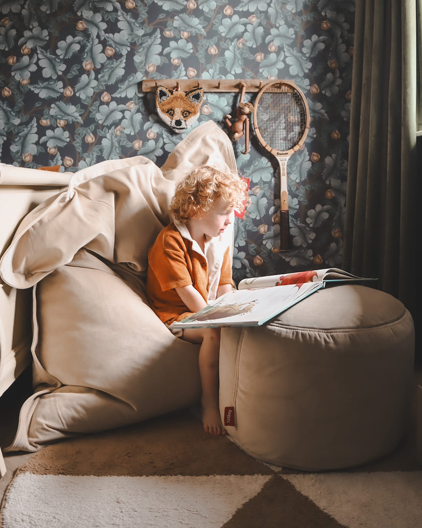 Child lounging on a soft Slim Velvet bean bag in a cozy corner, with books and headphones nearby.